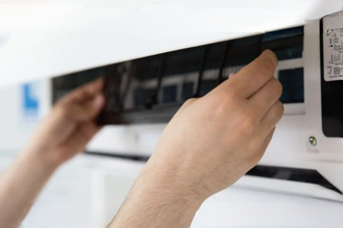 A person reaches into their heat pump to remove and clean their filter.