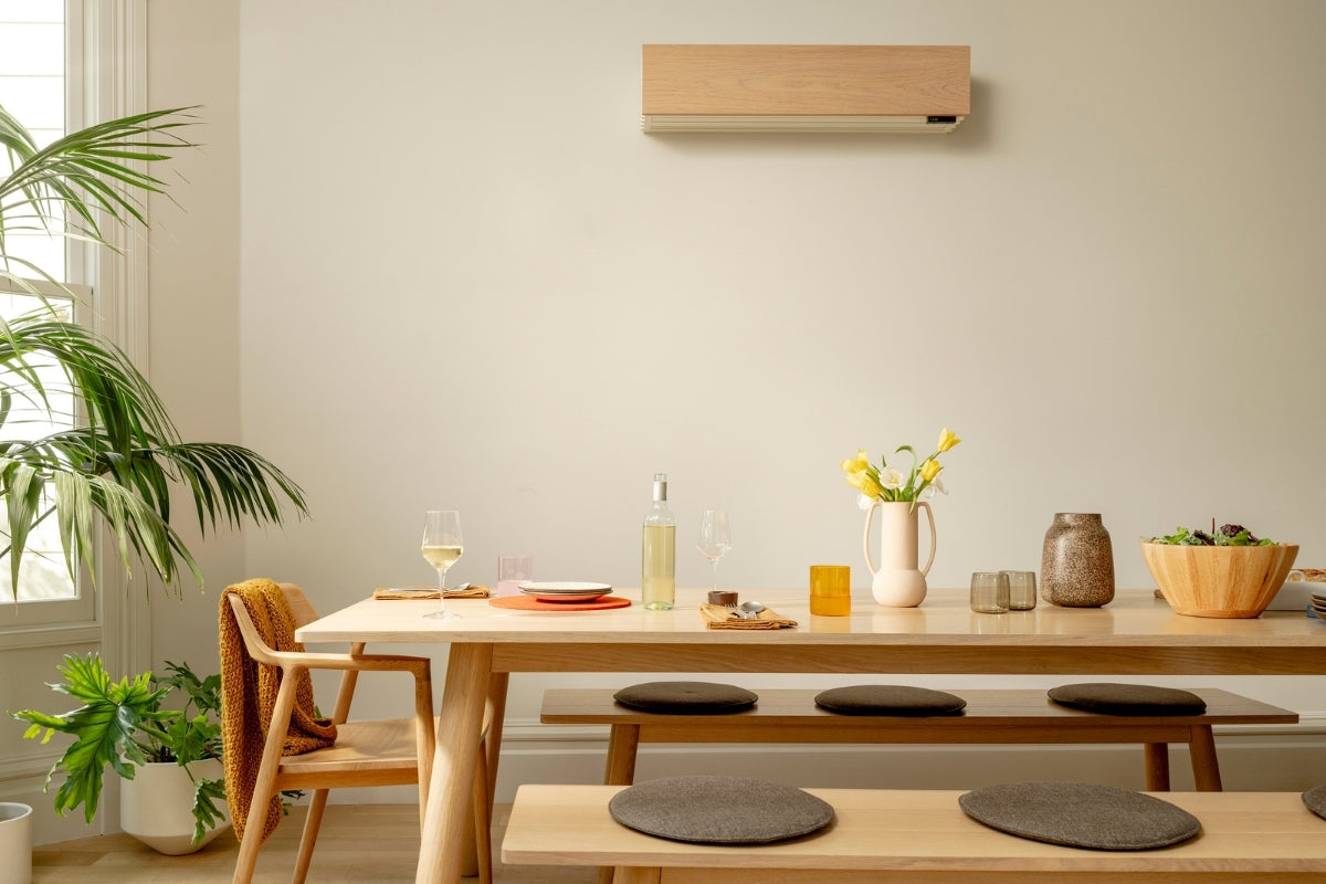 A Quilt heat pump hangs on the wall behind a dining room table and some house plants.