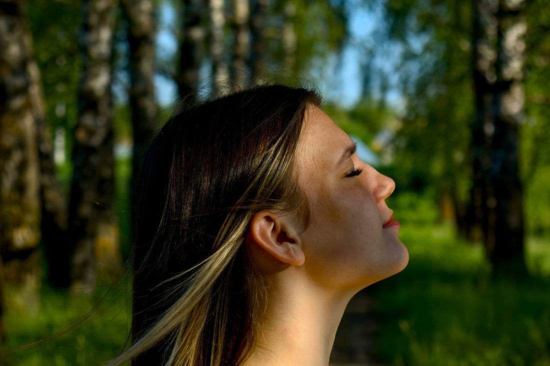 Someone takes a deep breath outdoors with a background of trees and long green grass.