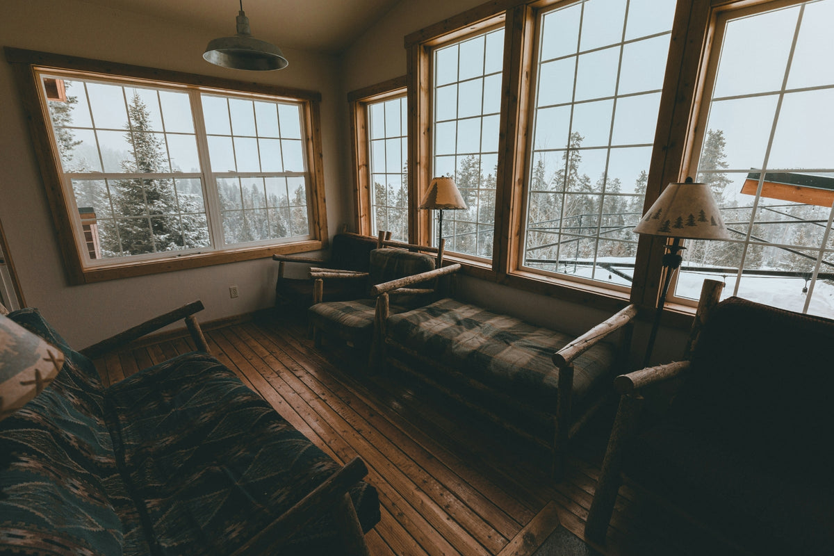 A room surrounded by windows looks out on a wintery scene with snow on the ground and evergreens dusted in snow.