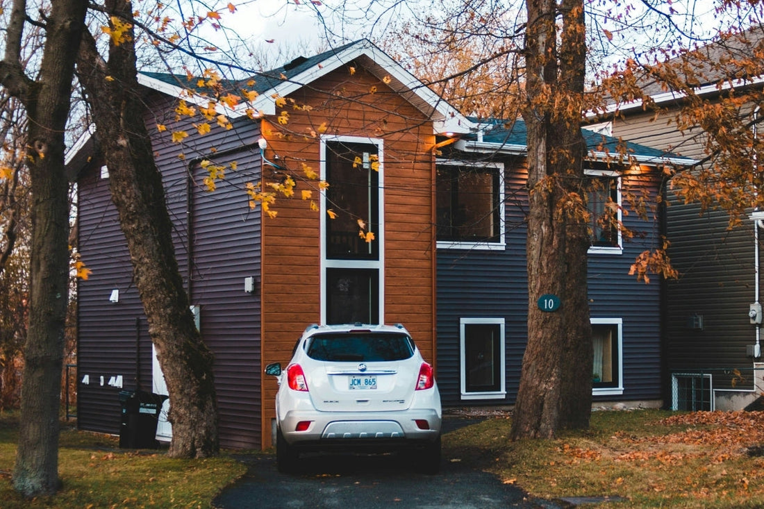 A car is parked outside of a modern home in the middle of fall.