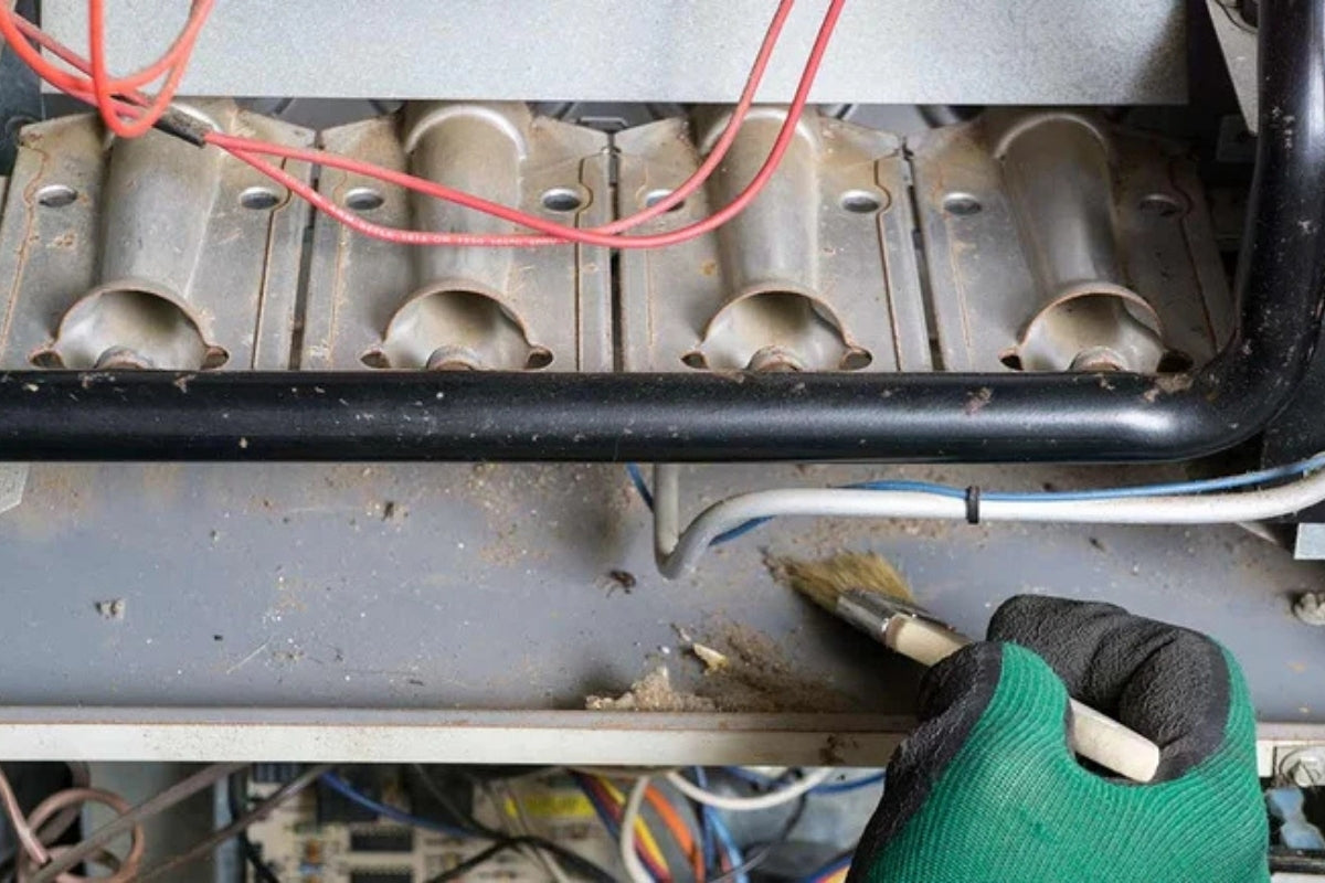 Someone wearing green work gloves brushes dust out of an HVAC system.