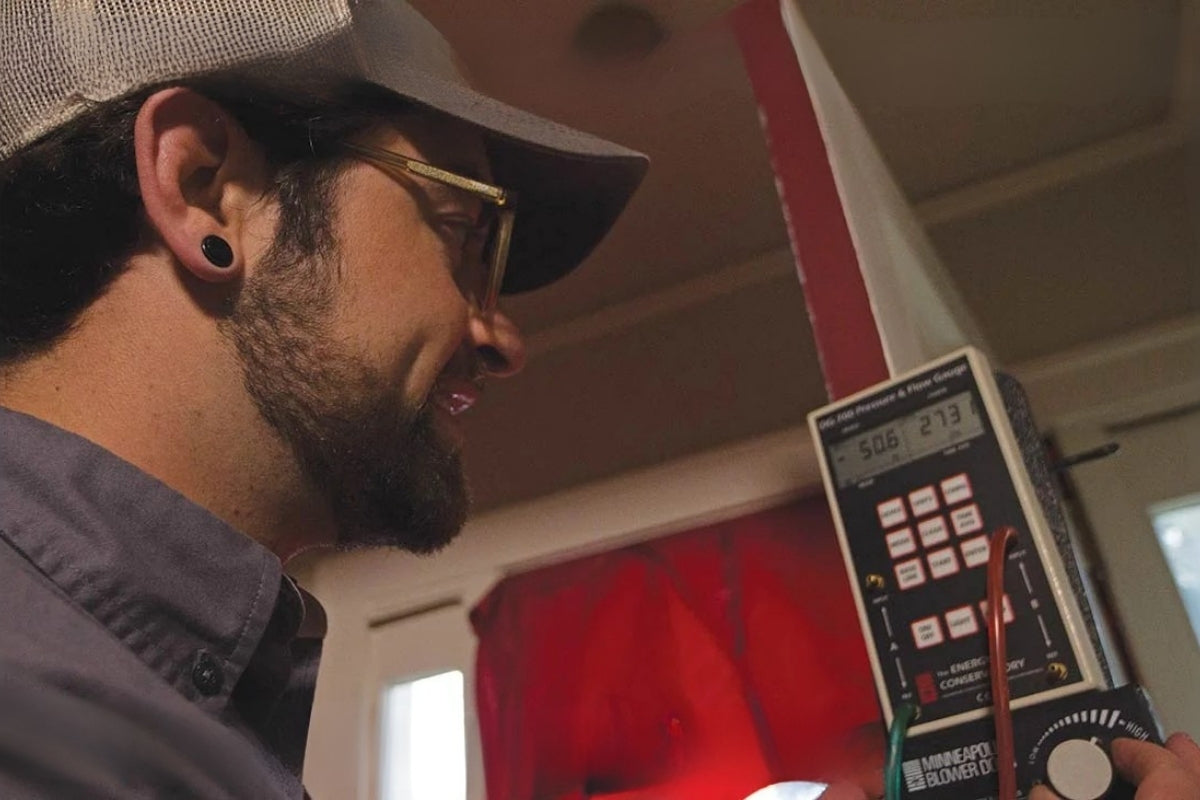 Technician conducting a home energy audit using a Minneapolis Blower Door test kit to measure air leakage and pressure, highlighting energy efficiency and home performance testing.