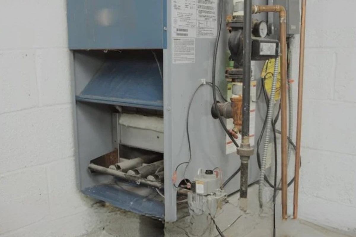 An old furnace sitting on top of cinder blocks in a basement with white walls.