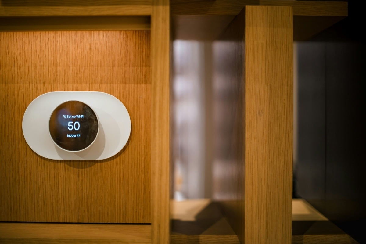 A smart thermostat is mounted on a wooden paneled wall.